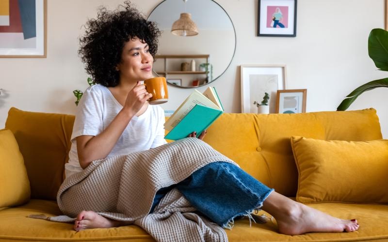 woman on a couch holding a cup and a book